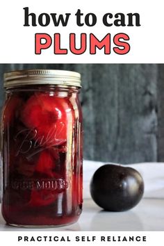 a jar filled with plums sitting on top of a table next to an apple