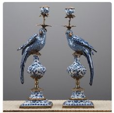 two blue and white bird figurines sitting on top of each other next to candlesticks