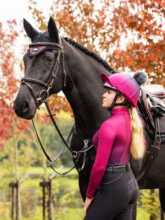 a woman standing next to a black horse wearing a pink hat and riding gear on it's head