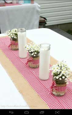 three mason jars filled with baby's breath daisies on a red and white checkered table runner