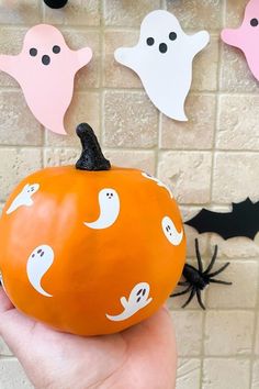 a hand holding an orange pumpkin with ghost faces on it and bats hanging from the wall