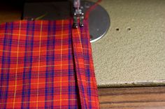 an orange and blue checkered fabric is next to a sewing machine with a needle