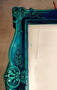 an ornate blue mirror sitting on top of a wooden floor next to a tiled wall