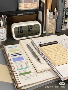 an open notebook sitting on top of a desk next to a clock and alarm clock