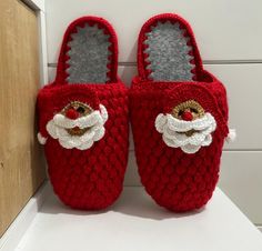 a pair of red knitted slippers with santa clause on the front and bottom