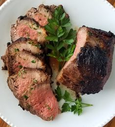 a white plate topped with sliced meat and garnished with parsley on top