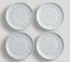 four white plates sitting on top of each other in front of a gray wall and floor