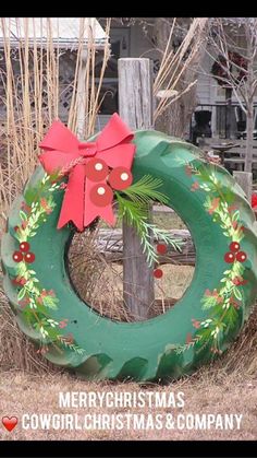 a green wreath with a red bow on it sitting in front of a wooden fence