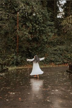 a woman standing in the rain with her arms spread out and she is wearing a white dress