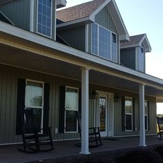 two rocking chairs sitting on the front porch of a large house with covered porches