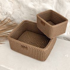 two wicker baskets sitting next to each other on a white surface with dried grass in the background