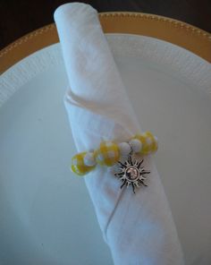 a white plate topped with a yellow and white napkin next to a silver sun brooch