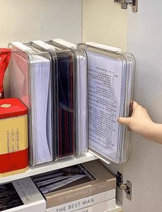 a hand is pointing at files on a shelf in a filing cabinet that holds several folders