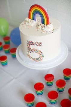 a white cake with rainbow frosting surrounded by red and green cupcakes on a table