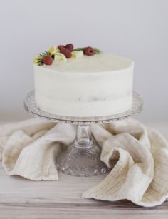 a white cake sitting on top of a glass cake platter next to a towel