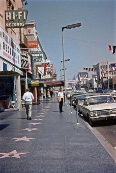 people walking on the sidewalk in front of shops and cars parked along the side walk