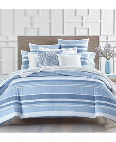 a bed with blue and white comforters in a room next to a vase filled with flowers