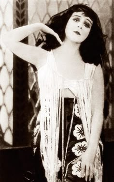 a black and white photo of a woman with her hand on her hip, leaning against a wall