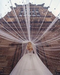 a woman in a wedding dress is standing with her veil over her head and looking up at the sky