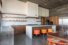 an open kitchen and dining room area with wood paneling, marble counter tops, and orange chairs