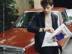 a man standing next to a red car and reading a paper with the word pass on it