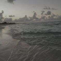 the beach is empty with waves coming in to shore and dark clouds are seen above