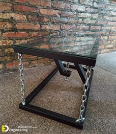 a glass table with chains on the bottom and chain around it's legs, sitting in front of a brick wall