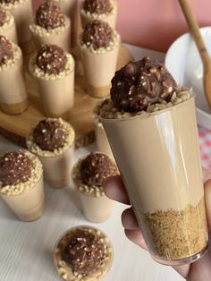 mini cheese cake in a cup being held up by someone's hand with other small desserts behind it