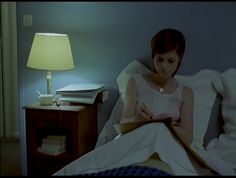 a woman sitting in bed reading a book with a lamp on the side table behind her