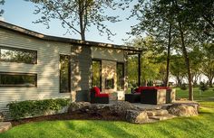 a house with some red chairs in front of it and trees around the back yard