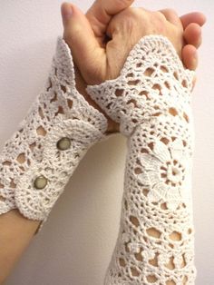 two white crocheted arm warmers with holes in the middle, one being held by someone's hand