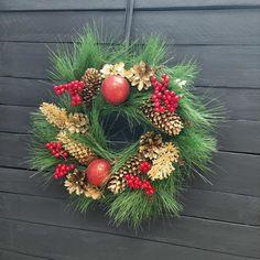 a wreath with pine cones and berries hanging on the side of a building in front of a wooden wall