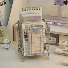 a wire basket holding magazines on top of a white desk next to a mouse and keyboard