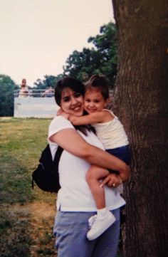 a woman and child hugging each other in front of a tree