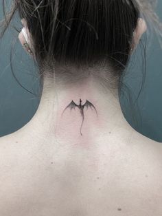 a woman's back neck with a small tattoo of two bats on her left side