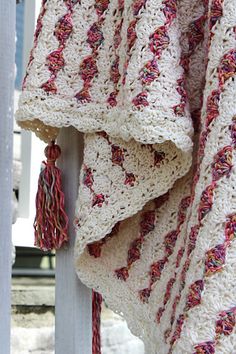 a crocheted blanket is hanging on a white pole with red tassels