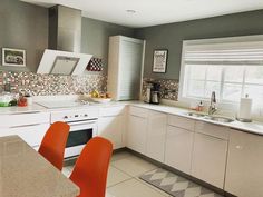 a kitchen with white cabinets and orange chairs next to the counter top, is seen in this image