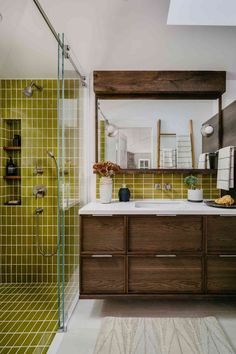 a green tiled bathroom with wooden cabinets and white counter tops, along with a large mirror on the wall