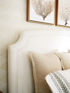 two framed pictures on the wall above a bed with white linens and decorative pillows