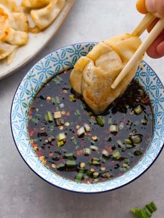 a person dipping food into a bowl with chopsticks