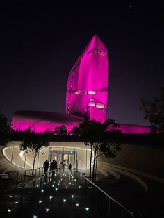 people are walking up and down the stairs in front of a building with pink lights