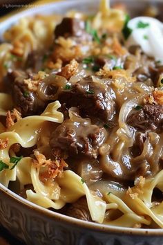 a close up of a bowl of food with noodles and meat in sauce on the side