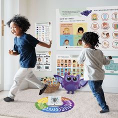 two children playing with toys on the floor in front of a white wall and posters