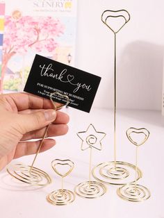 a hand holding a thank you card next to some small metal hearts and spirals