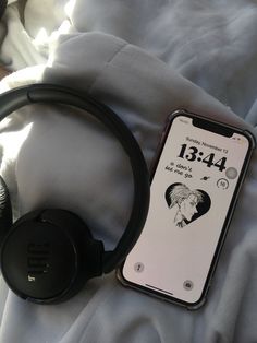 an iphone with headphones on top of it sitting on a bed next to a pair of headphones