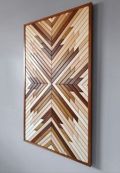 a wooden wall hanging on the side of a gray wall with an abstract design made out of wood strips