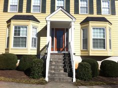 a yellow two story house with black shutters on the front and stairs leading up to it