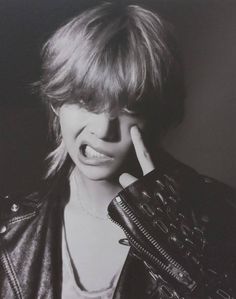 a black and white photo of a woman holding her hand up to her face while wearing a leather jacket