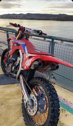 a red dirt bike parked on the side of a road next to a body of water