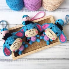 three crocheted stuffed animals sitting on top of a wooden tray next to skeins of yarn